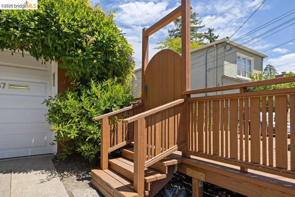 Wood-tone entry gate and railing system with steps, featuring an arched arbor draped in established foliage