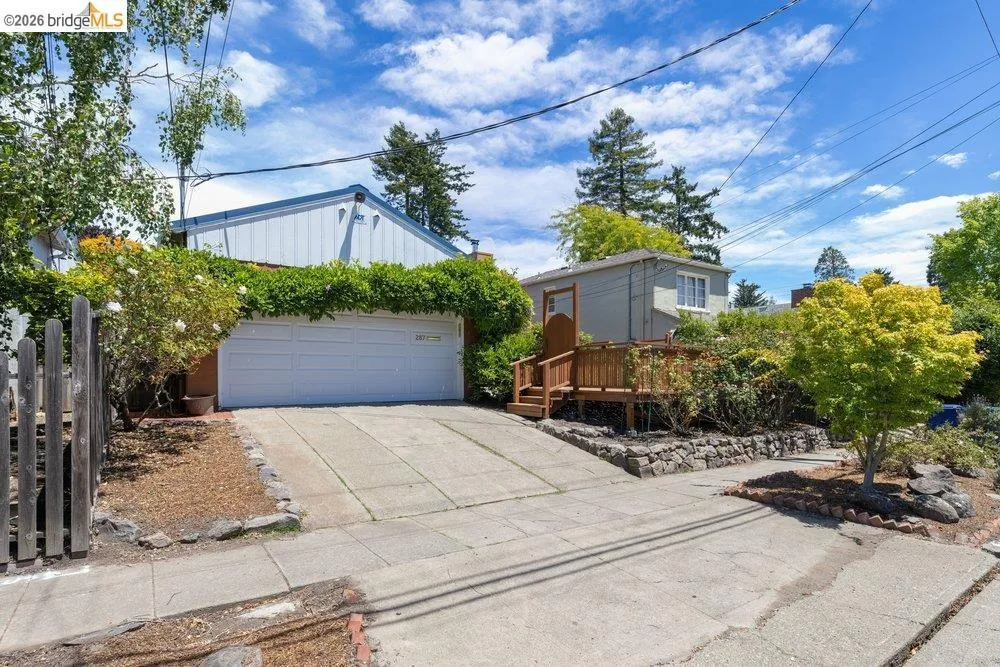 Property exterior featuring a two-car garage with a concrete driveway, a wooden deck, and established landscaping