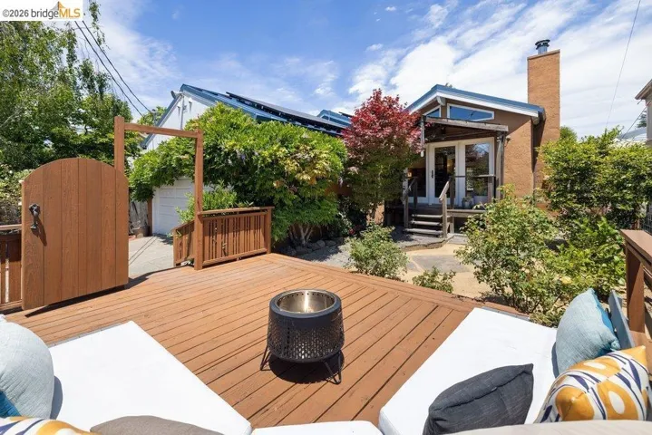 Spacious outdoor deck featuring wood decking, a built-in fire pit, and mature perimeter landscaping
