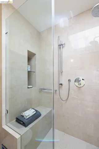 Glass-enclosed shower featuring large format wall tiles, a built-in bench, and a recessed niche with shelving