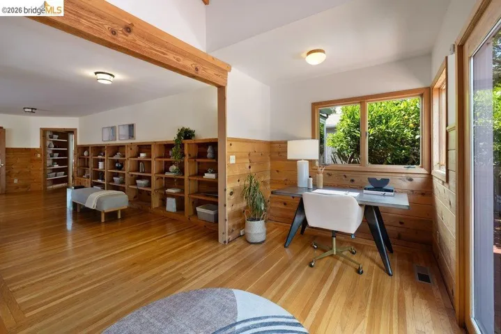 Wood-finish flooring throughout, featuring extensive built-in shelving, natural wood wainscoting, and large windows with outdoor scenery