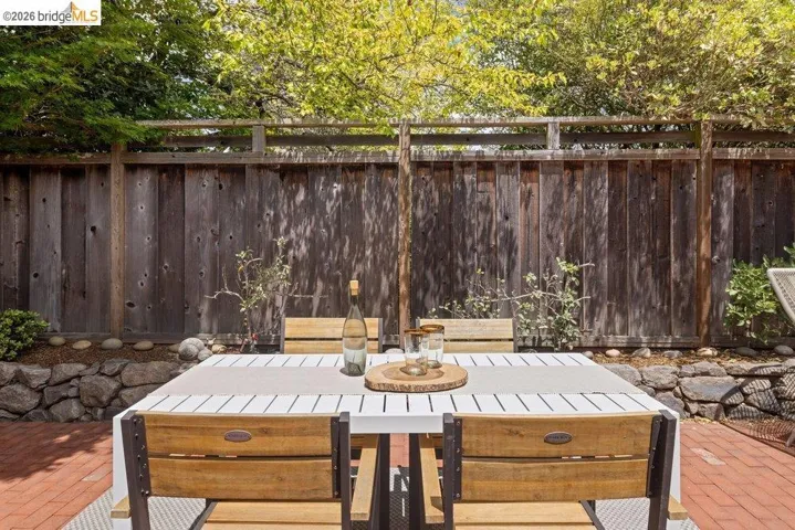 Brick patio featuring a wooden privacy fence, stone retaining wall, and mature landscaping