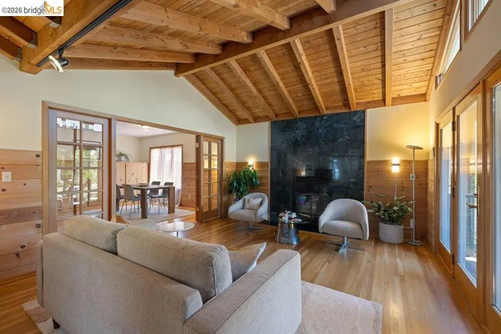 Living area featuring a vaulted wood-plank ceiling, wood-finish flooring, a dark stone fireplace, and wood-paneled walls
