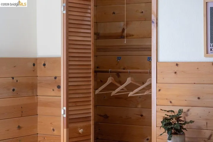 Built-in closet featuring louvered bi-fold doors, natural wood paneling, and a wood hanging rod