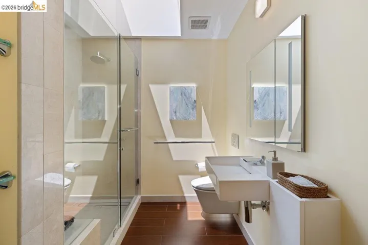 Contemporary bathroom featuring a floating vanity with an integrated sink, a frameless glass shower enclosure, wood-finish flooring, and a skylight