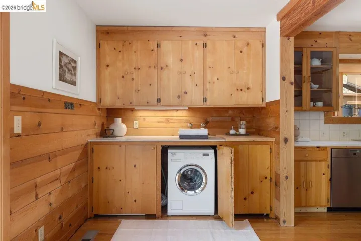 Laundry station featuring wood-paneled walls and cabinetry, under-cabinet lighting, a built-in sink, and a front-loading appliance