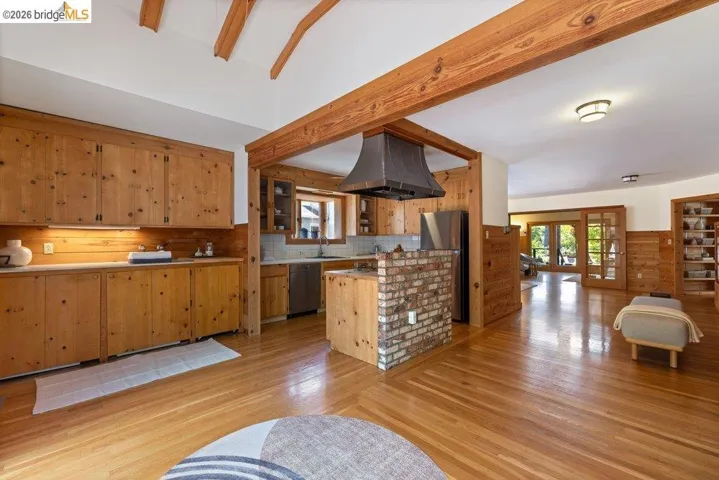 Warm wood-finish flooring complements the exposed wood beams and paneling throughout this open-concept kitchen and living area