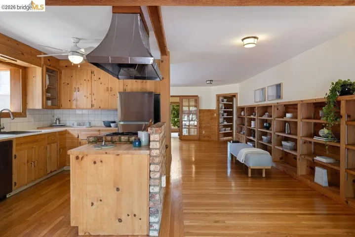 Open-concept kitchen and living area featuring extensive wood-finish flooring, wood cabinetry, a built-in range, and a stainless steel range hood