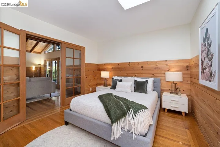 Bedroom featuring wood-paneled walls, hardwood flooring, and a skylight