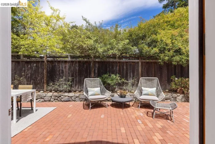 Brick paver patio featuring a wooden privacy fence, stone retaining wall, and mature trees