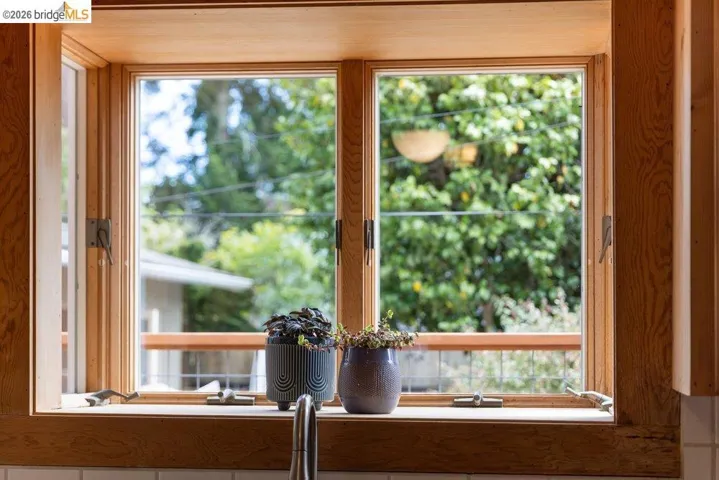 Double-hung casement windows featuring natural wood framing and trim above a white tile backsplash and a stainless steel faucet