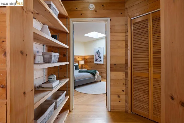 Wood-paneled hallway featuring built-in shelving, louvered closet doors, and hardwood flooring