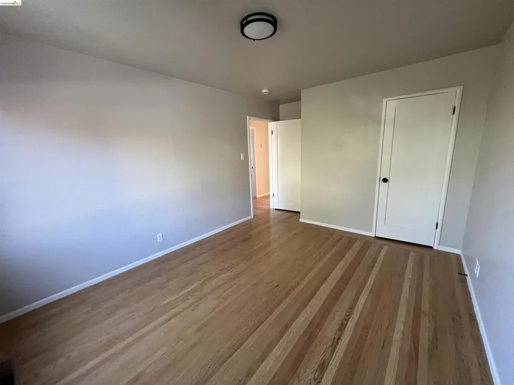 Hardwood flooring throughout a room featuring a modern flush-mount ceiling light and white doors with matte black hardware