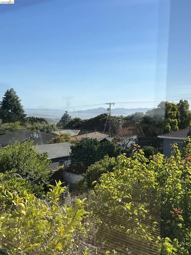 Distant cityscape and water views visible over surrounding rooftops and abundant foliage