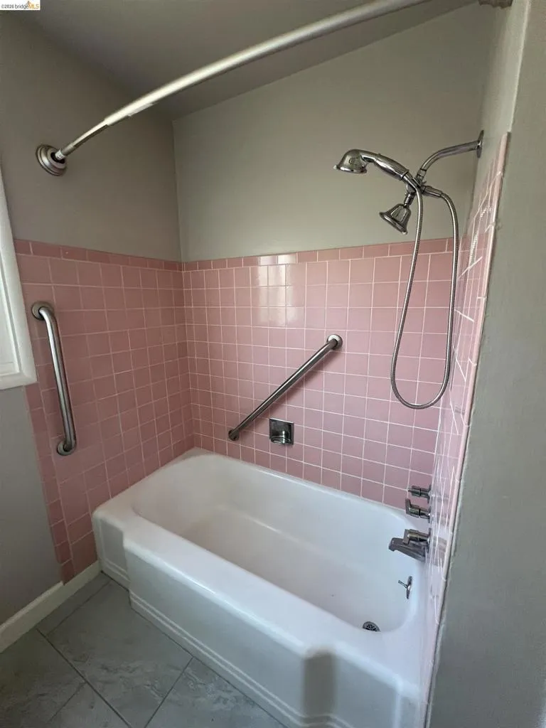 Bathroom featuring a white bathtub, pink tiled walls, and a chrome dual shower head fixture