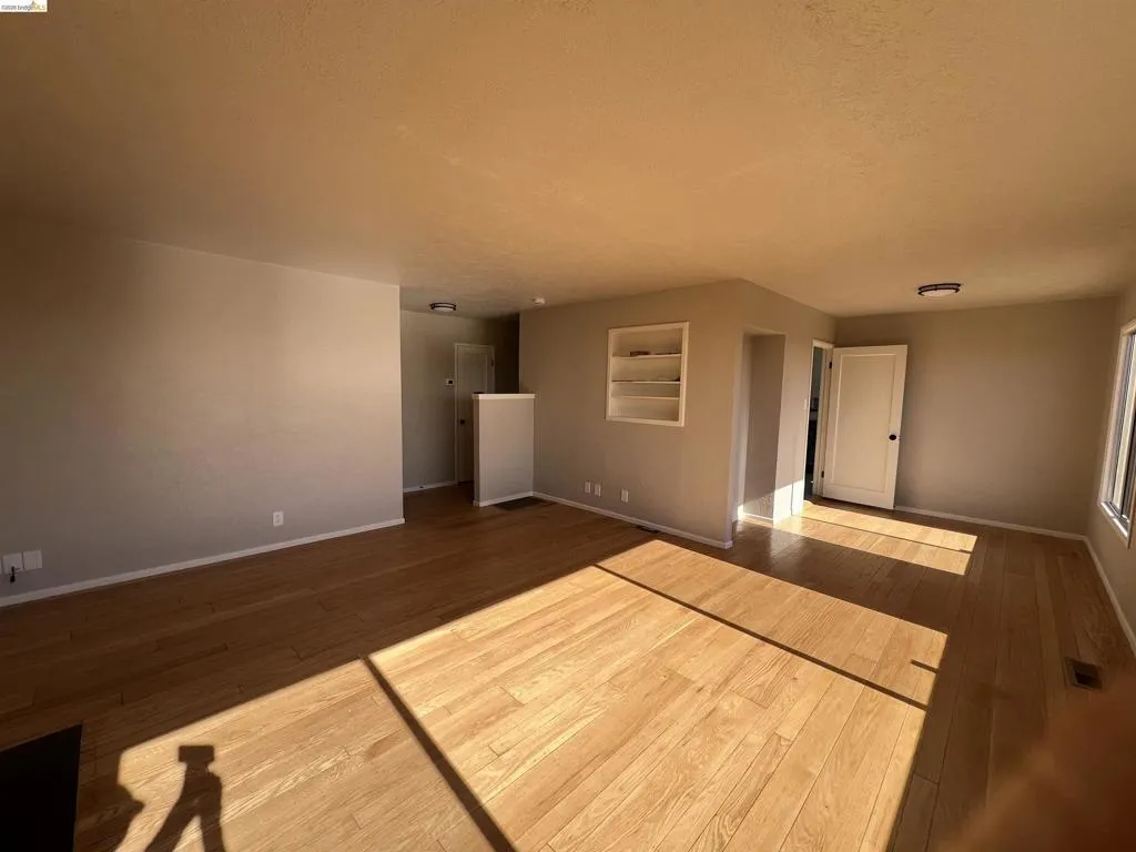 Expansive interior featuring wood-finish flooring, built-in shelving, white trim, and a white interior door with dark hardware