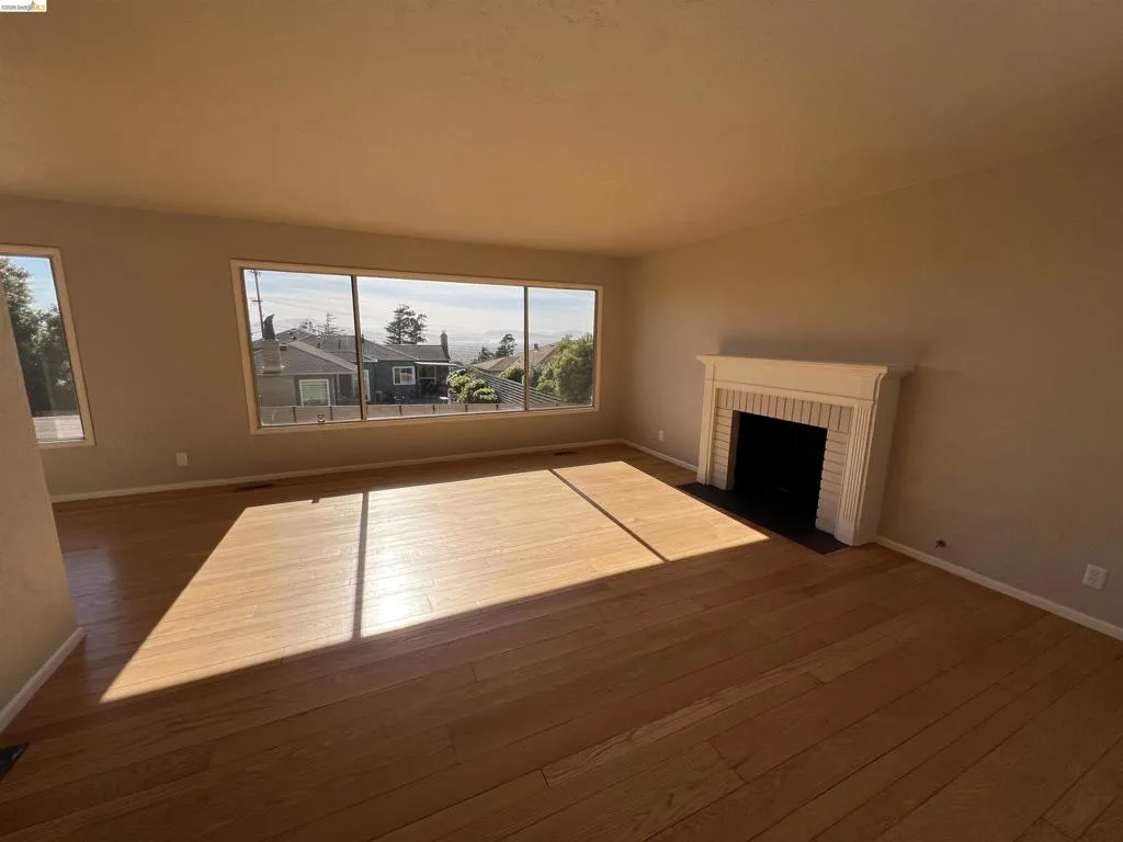 Spacious interior room featuring extensive wood-finish flooring, a classic fireplace with a white mantel, and large picture windows