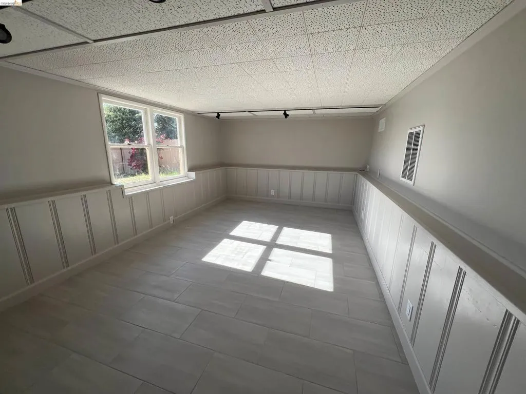 Versatile interior space featuring light wood-finish flooring, wainscoting, and a drop ceiling with recessed track lighting