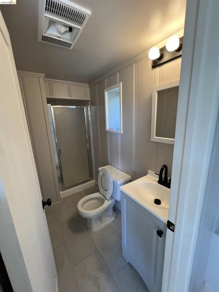 Bathroom featuring a modern vanity with integrated sink, black fixtures, rectangular wall-mounted mirror, white paneling, and tile flooring