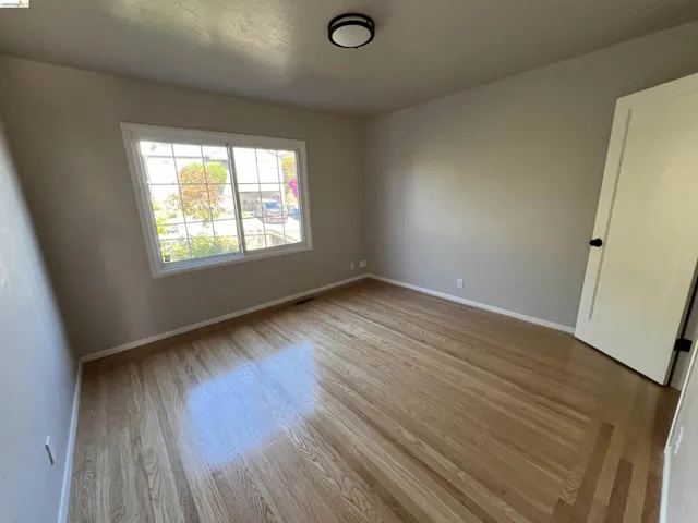 Hardwood flooring throughout featuring white baseboards, a flat-panel door with matte black hardware, and a contemporary flush-mount ceiling light