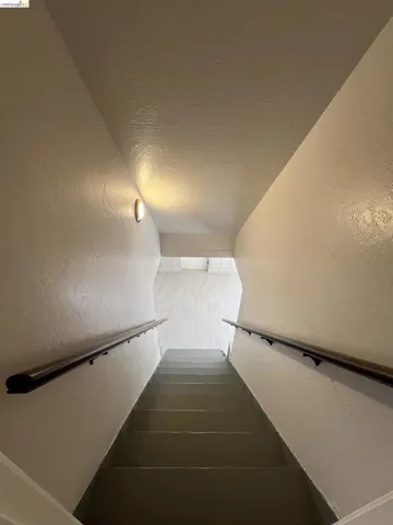 Stairwell featuring solid treads, wall-mounted handrails, and a modern sconce providing illumination