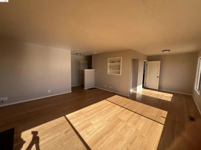 Expansive interior featuring wood-finish flooring, built-in shelving, white trim, and a white interior door with dark hardware