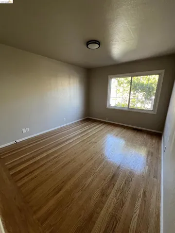 Spacious room featuring wood-finish flooring, a contemporary flush-mount ceiling light, a large window, and neutral wall tones
