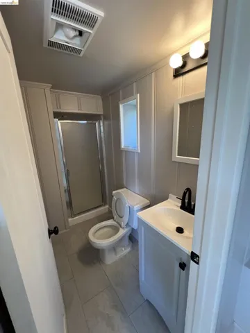 Bathroom featuring a modern vanity with integrated sink, black fixtures, rectangular wall-mounted mirror, white paneling, and tile flooring