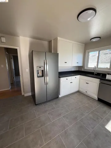 Kitchen featuring contemporary tile flooring, white cabinetry, dark countertops, a stainless steel refrigerator, and a stainless steel dishwasher