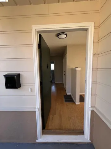 Entryway featuring a black mailbox, light-colored siding, a dark door, and wood-finish flooring