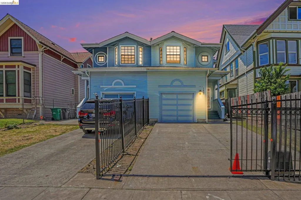 Light blue stucco exterior featuring a two-car garage with horizontal paneling, two prominent bay windows, and a concrete driveway