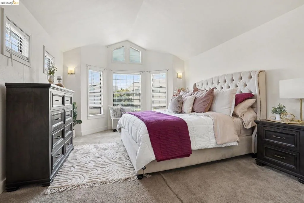 Carpeted bedroom featuring a bay window with multiple panes, vaulted ceiling, and recessed lighting