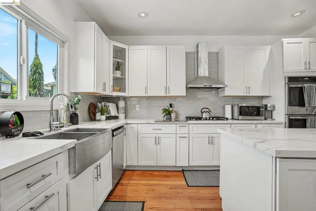 Modern kitchen with white shaker cabinetry, stainless steel farmhouse sink, white countertops, stainless steel appliances, and wood-finish flooring