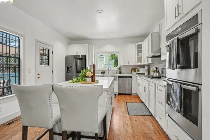 Open-concept kitchen featuring white cabinetry, stainless steel appliances, a center island with countertop seating, wood-finish flooring, and recessed lighting
