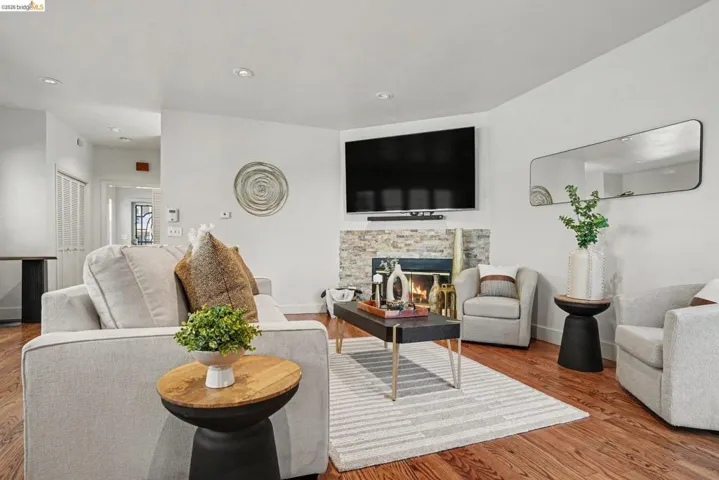 Living area featuring hardwood flooring, a stone-clad fireplace, recessed lighting, and white walls