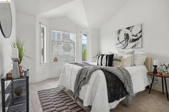 Vaulted ceiling bedroom featuring plush carpet flooring, a bay window with blinds, and white painted walls