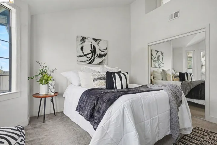 Bedroom featuring light-toned carpeting, a tall window with black framing, and white walls