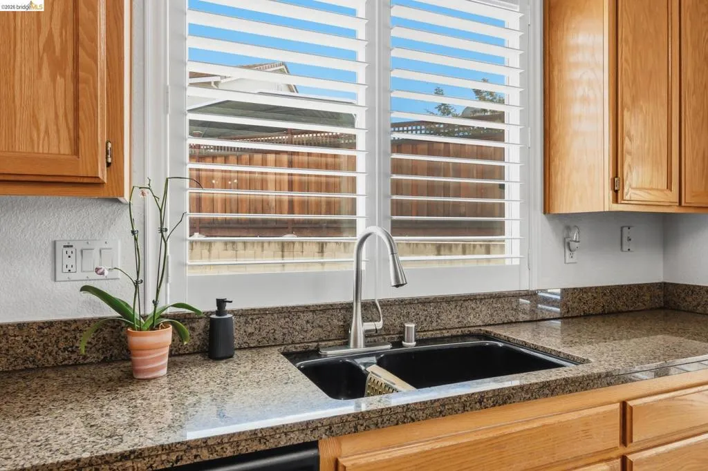 Kitchen featuring granite countertops, wood cabinetry, a dual basin sink with a high-arc faucet, and plantation shutters
