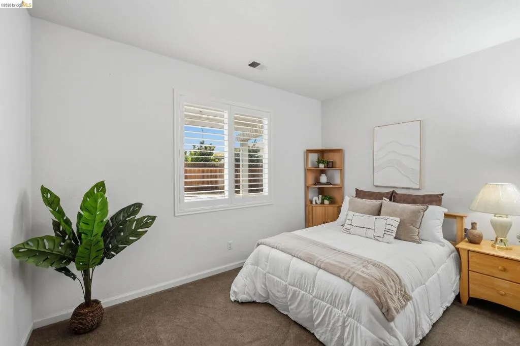 Bedroom featuring a window with white plantation shutters, neutral wall color, and brown carpet flooring