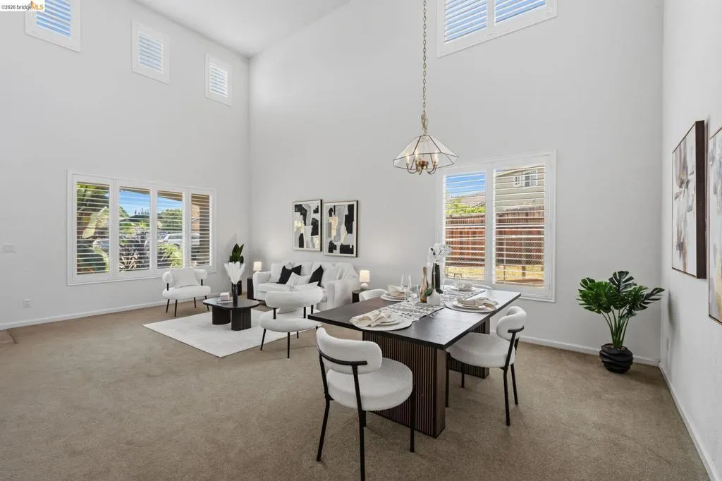 High ceilings defining a spacious room featuring multiple windows with plantation shutters, a chandelier, and carpet flooring