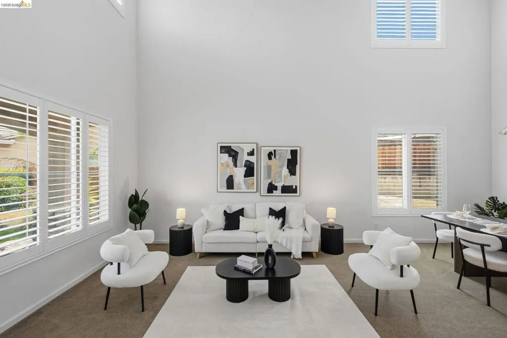 Vaulted ceiling living space featuring multiple windows with white plantation shutters, neutral-toned carpeting, and an open-concept dining area