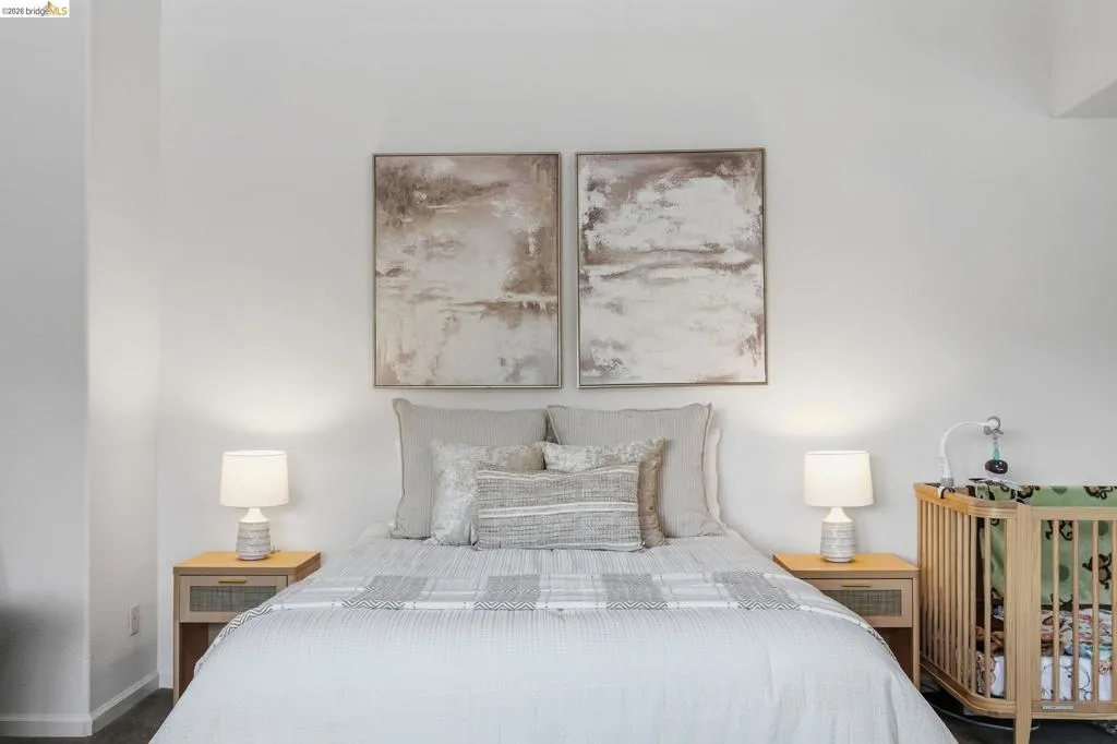 Recessed lighting illuminates a neutral palette bedroom featuring light-colored walls and wood-finish flooring