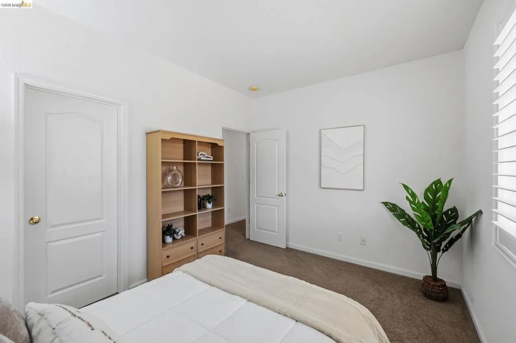 Bedroom featuring neutral carpeting, white walls, two paneled interior doors, and a window with white louvered blinds