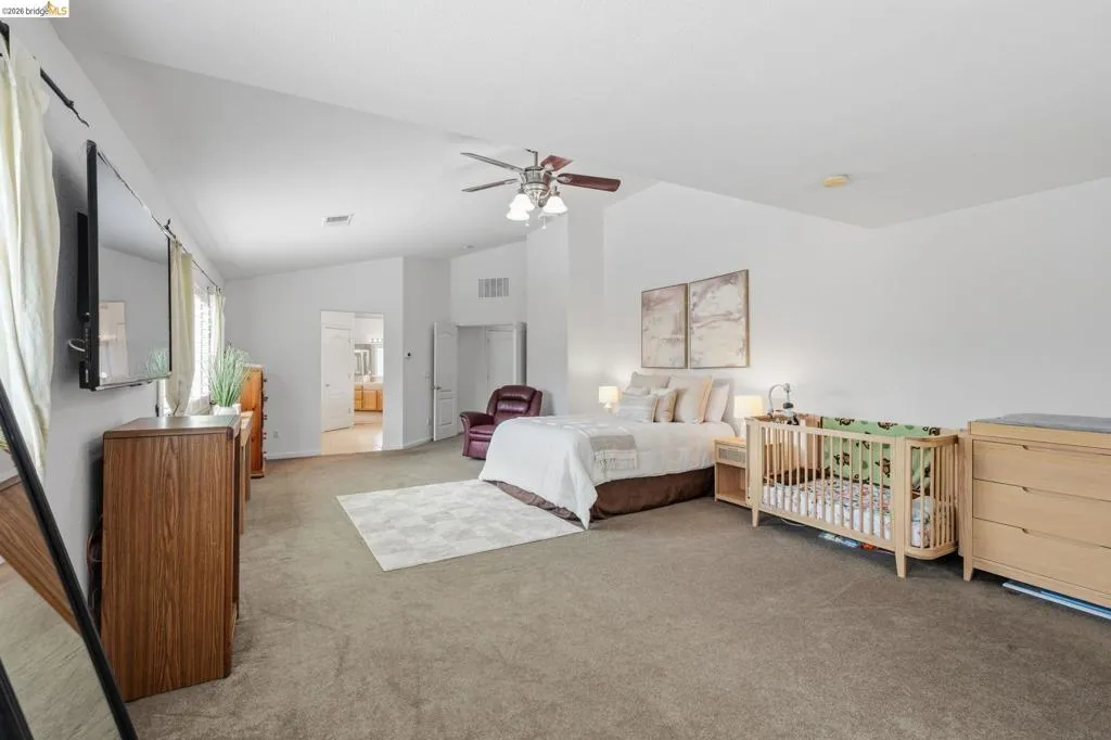 Spacious bedroom featuring vaulted ceilings, carpet flooring, a ceiling fan with integrated lighting, and multiple windows providing natural light