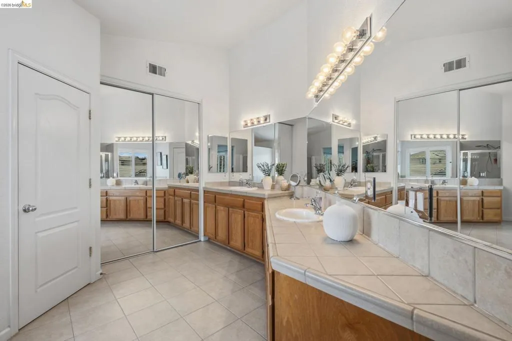 Spacious bathroom featuring a dual vanity with light wood cabinetry, tile countertops, and integrated sinks