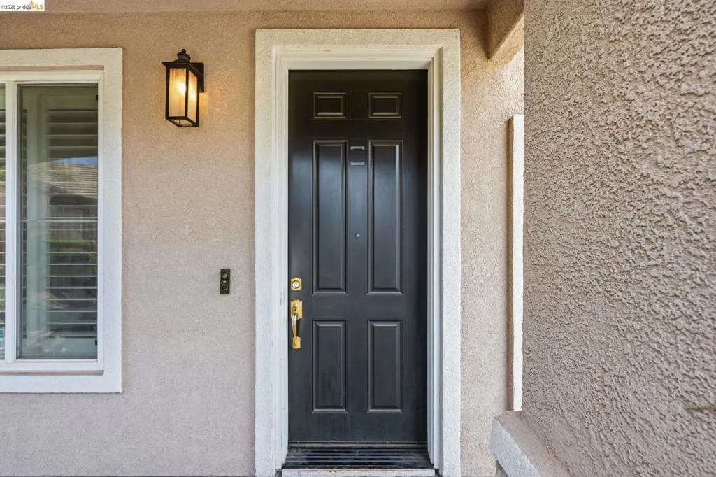 Entryway featuring a paneled door with polished brass hardware, a white-framed window with interior plantation shutters, and a black exterior sconce
