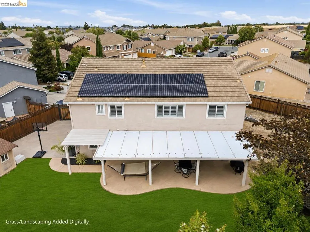 Rear exterior featuring a full-width covered patio with a solid roof, a manicured lawn, and solar panels