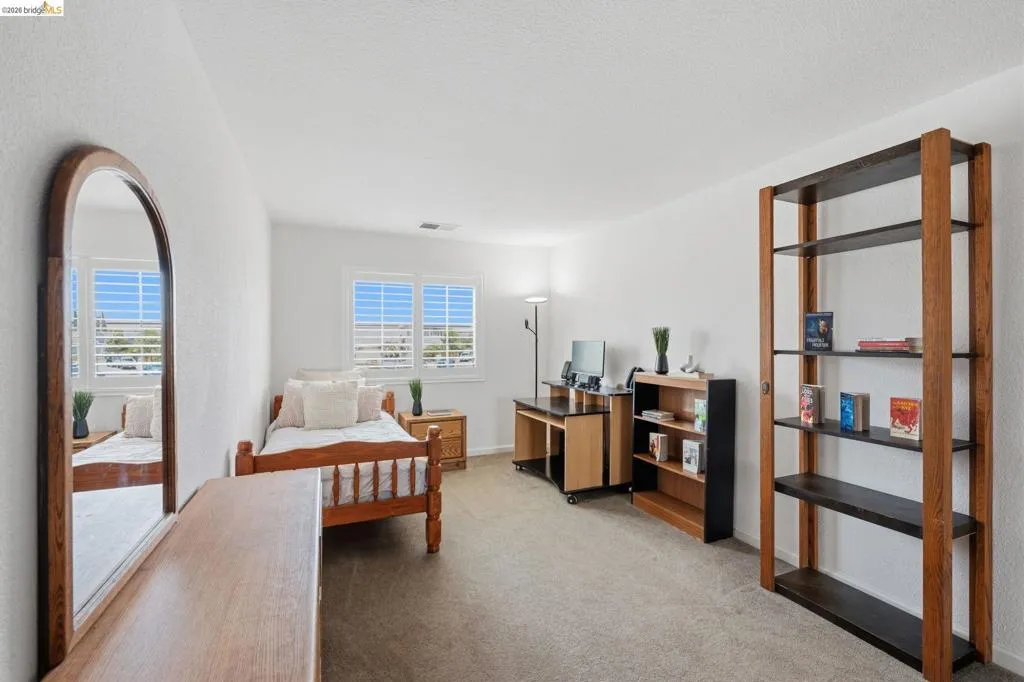 Carpeted room with white walls and a pair of windows featuring white plantation shutters