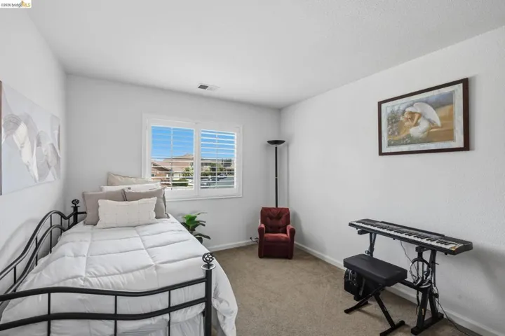 Carpeted room featuring a window with white plantation shutters, a textured ceiling, and light-colored walls