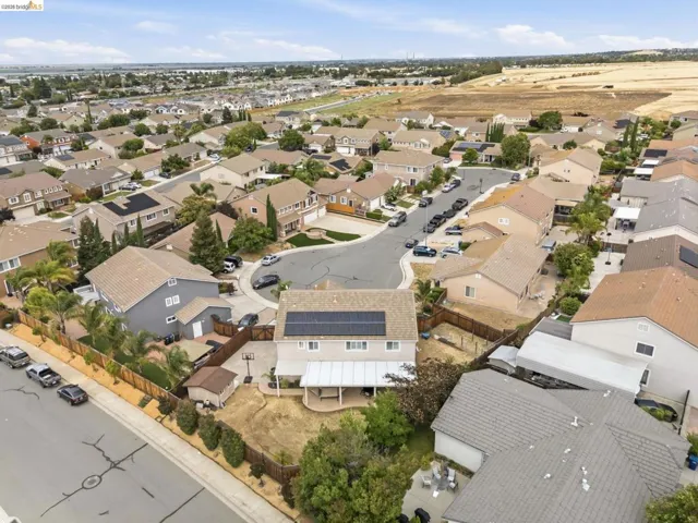 Two-story residential property with solar panels, an attached patio cover, a wooden perimeter fence, and a spacious backyard